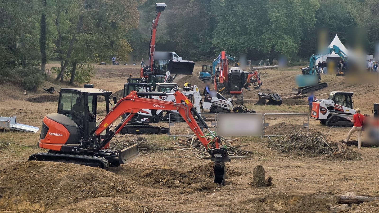 Une mini-pelle avec tiltrotateur creuse une tranchée sur le terrain de démonstration du Salonvert 2026 ; d'autres pelles et chargeurs derrière