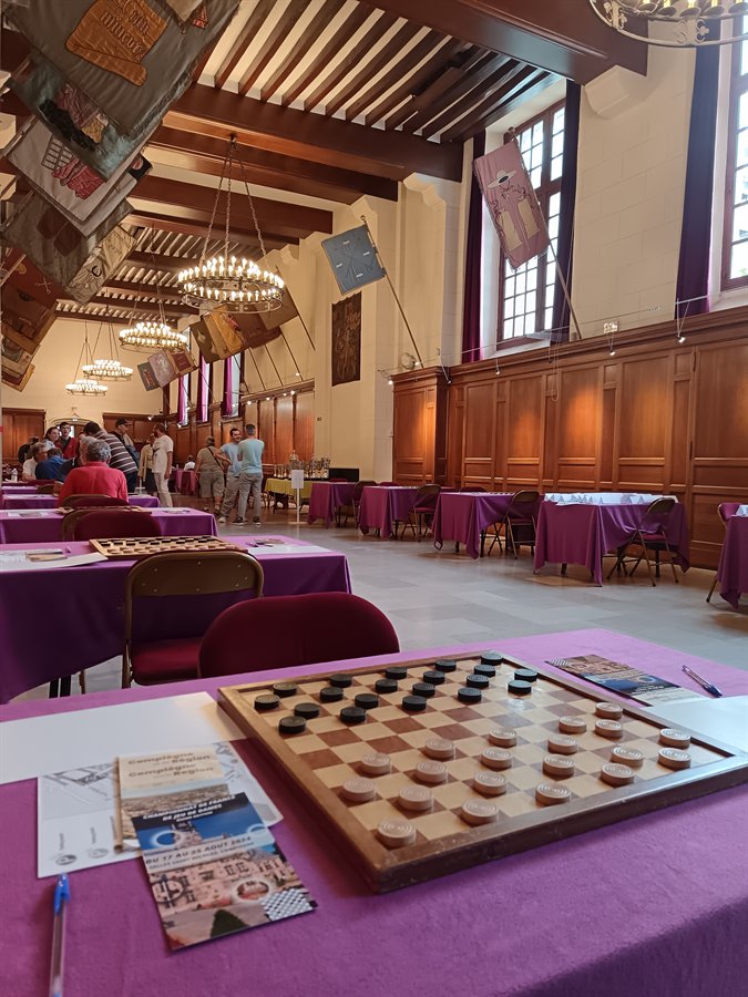 La grande salle du championnat de France de jeu de dames à Compiègne, les tables alignées et un damier au premier plan
