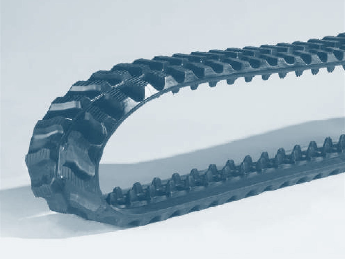 Motif de crampons de deux chenilles caoutchouc côte à côte, vu de près : barres transversales et pavés en relief