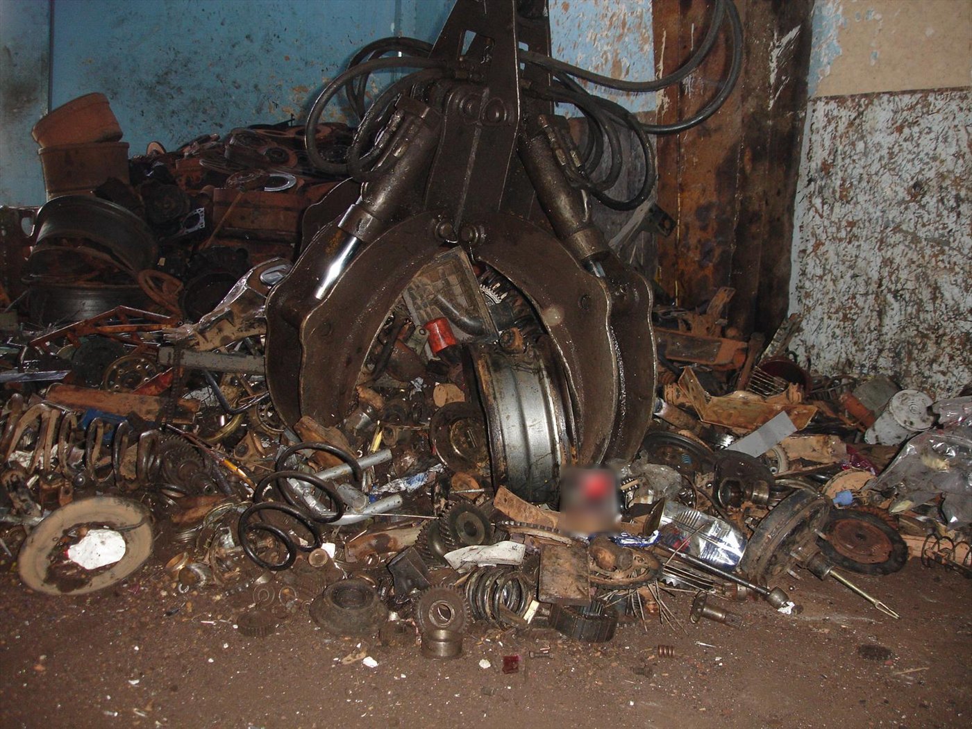 Grappin à plusieurs coquilles posé sur un tas de pièces métalliques en vrac, dans un hangar de ferrailleur.