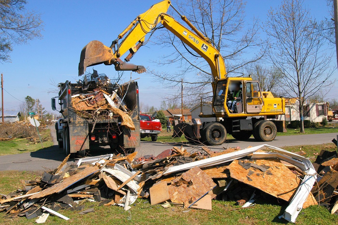 Pelle sur pneus jaune vidant dans un camion-benne un godet muni d'un pouce, chargé de débris de bois ; un tas de débris au premier plan.